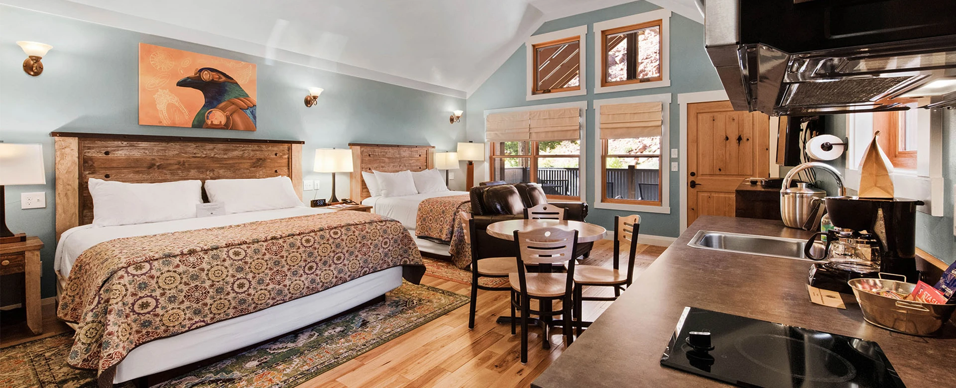 A wide view of a hotel room with two beds, a kitchenette, a table, a sofa, and a rug.