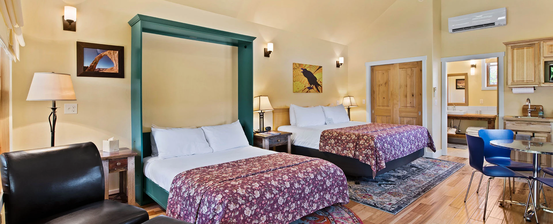 A hotel room with two beds, a desk, and a bathroom doorway.
