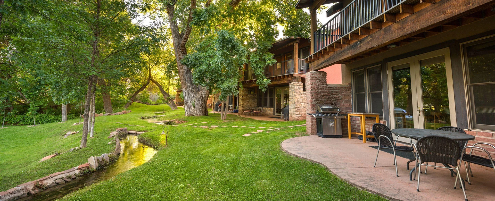 A patio area with a grill and outdoor seating next to a stream running through the property.