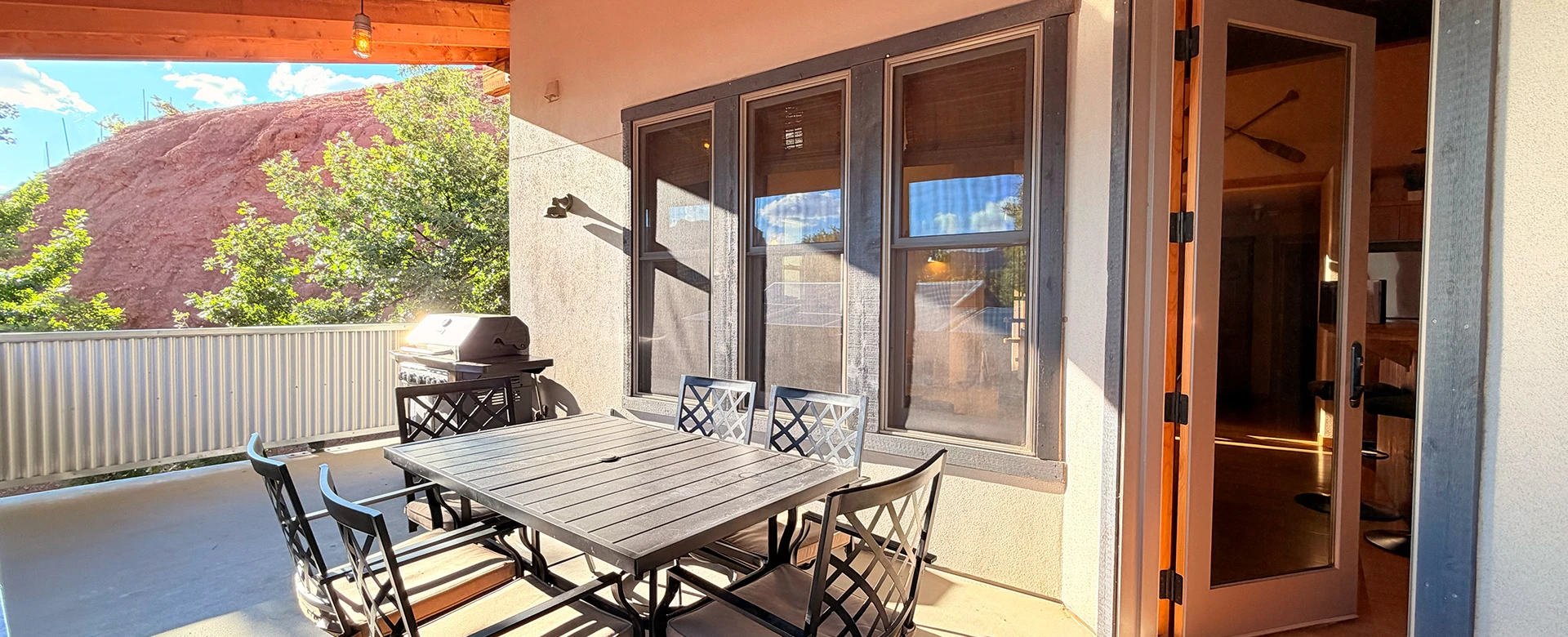 A patio with a dining table, chairs, and a grill, overlooking a mountain.